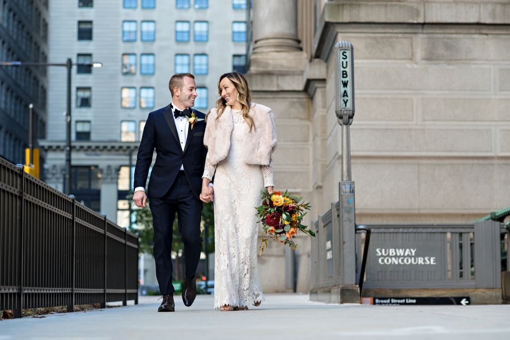 A bride and groom walk along City Hall next to the subway in Philadelphia.